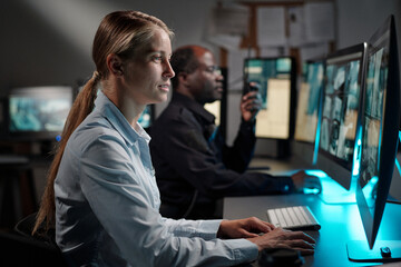 Young serious woman in uniform of security officer clicking mouse and looking at desktop computer screen with cctv video