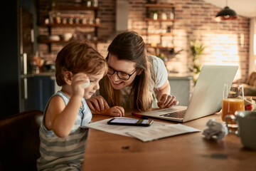 Mom working on laptop while spending time with toddler at breakfast table