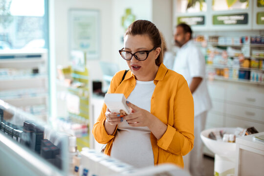 Pregnant woman reading medication label in pharmacy