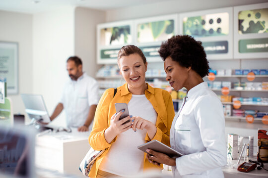 Female pharmacist helping pregnant woman in drug store
