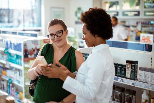 Female pharmacist helping pregnant woman in drug store