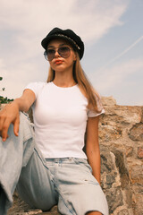 A woman is sitting on a rock wearing a white shirt and blue jeans