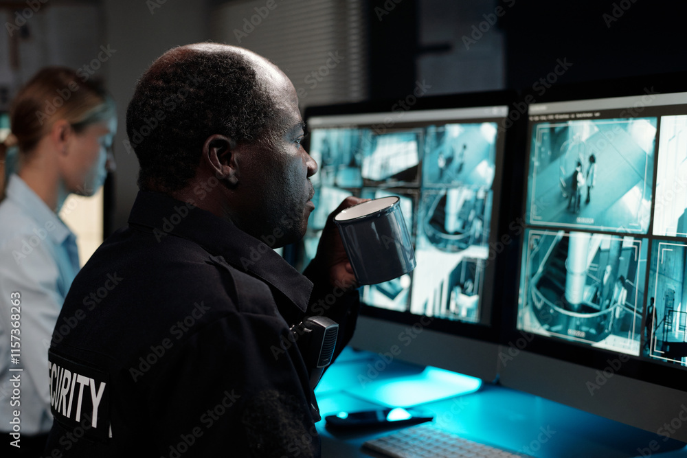 Poster serious mature male officer in uniform having cup of coffee while sitting in front of computer scree