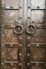 Fototapeta premium Rustic wooden doors with metal accents and large knockers in an ancient style located in a historic building