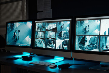Screens of desktop computers with cctv videos on screens standing in row on workplace of officers in observation room