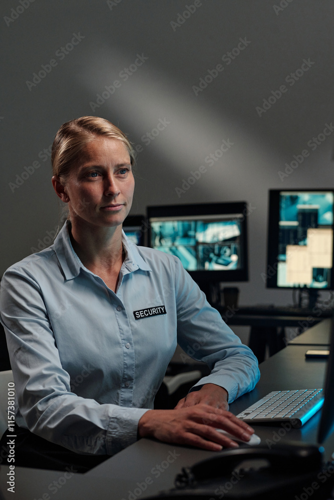 Poster young blond female security guard or officer of observation room sitting by desk and clicking mouse 