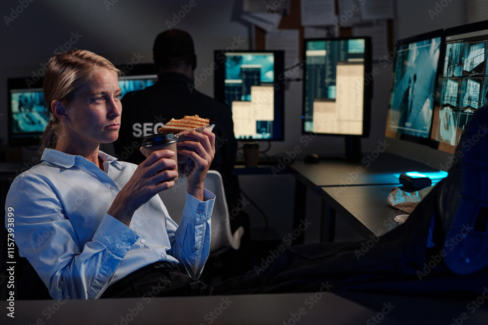 Poster young security guard with cup of coffee and sandwich sitting in front of computer monitor with cctv 