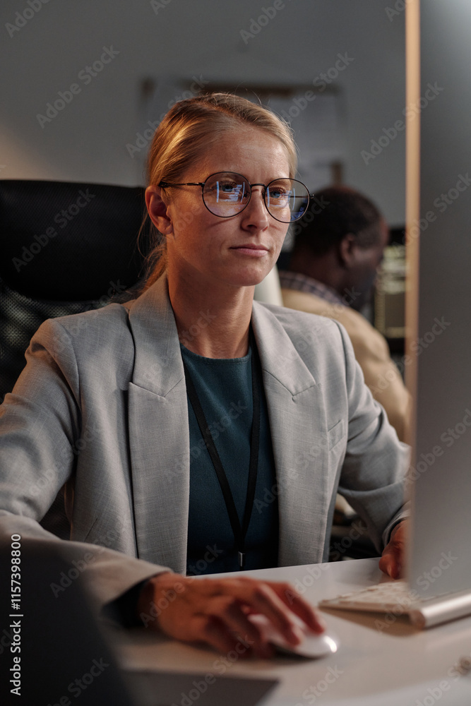 Poster Young blond female programmer clicking mouse and looking at computer screen while fixing technical error in coworking space
