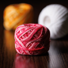Skeins of colored melange threads in white, pink and yellow lie on a dark wooden table. Selective...