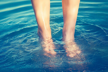 female feet in the water, beautiful bright blue water, texture of the blue water surface