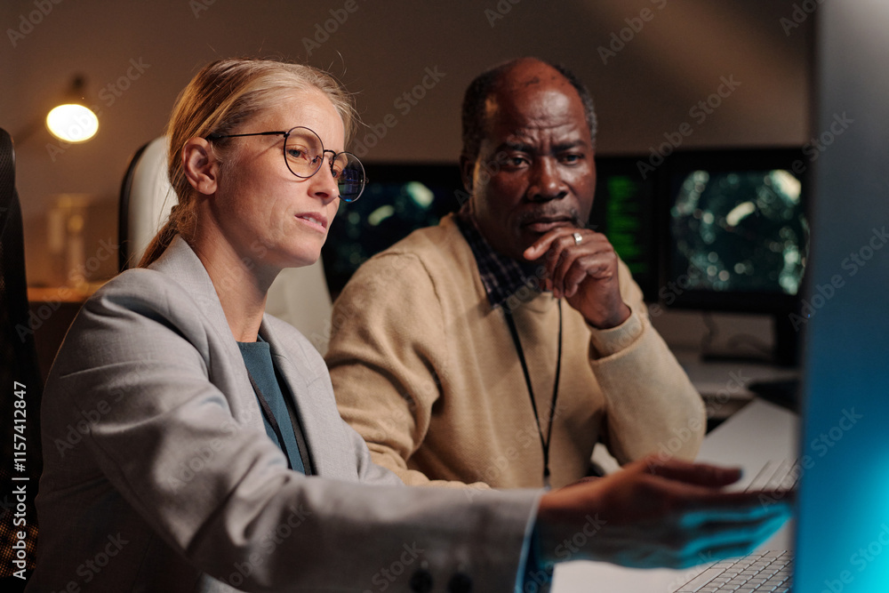 Poster young confident blond female it engineer pointing at computer screen while explaining male colleague