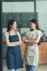 Coffee Shop Conversations: Two smiling women wearing aprons stand in a cozy cafe, chatting and connecting over a shared passion for coffee.