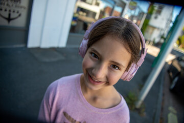 Smiling girl enjoys music while wearing pink headphones outdoors. A young girl with a joyful expression listens to music through her pink headphones in a vibrant, urban environment filled with colorfu