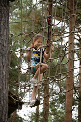 A child navigates a challenging ropes course, showing determination and focus while surrounded by tall trees in a lush outdoor setting.