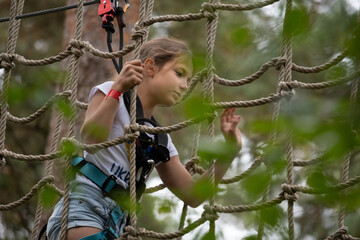 A young girl confidently navigates a treetop ropes course, surrounded by vibrant leaves and the tranquility of nature, embracing her adventurous spirit.