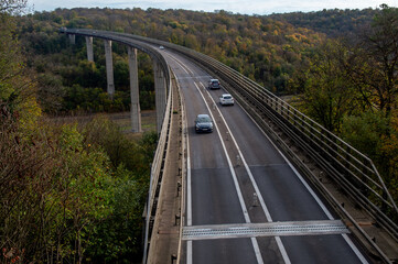 des voitures circulent sur un viaduc qui relie une vallée avec des arbres en automne