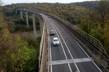des voitures circulent sur un viaduc qui relie une vallée avec des arbres en automne