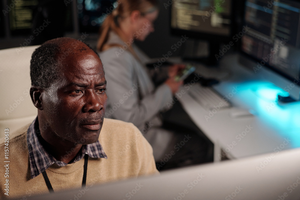 Poster Serious experienced IT engineer looking at desktop computer screen while decoding online data or developing new software