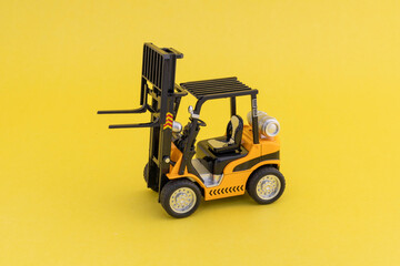 Toy forklift loader with raised up elevator on yellow background. Copy space for text.