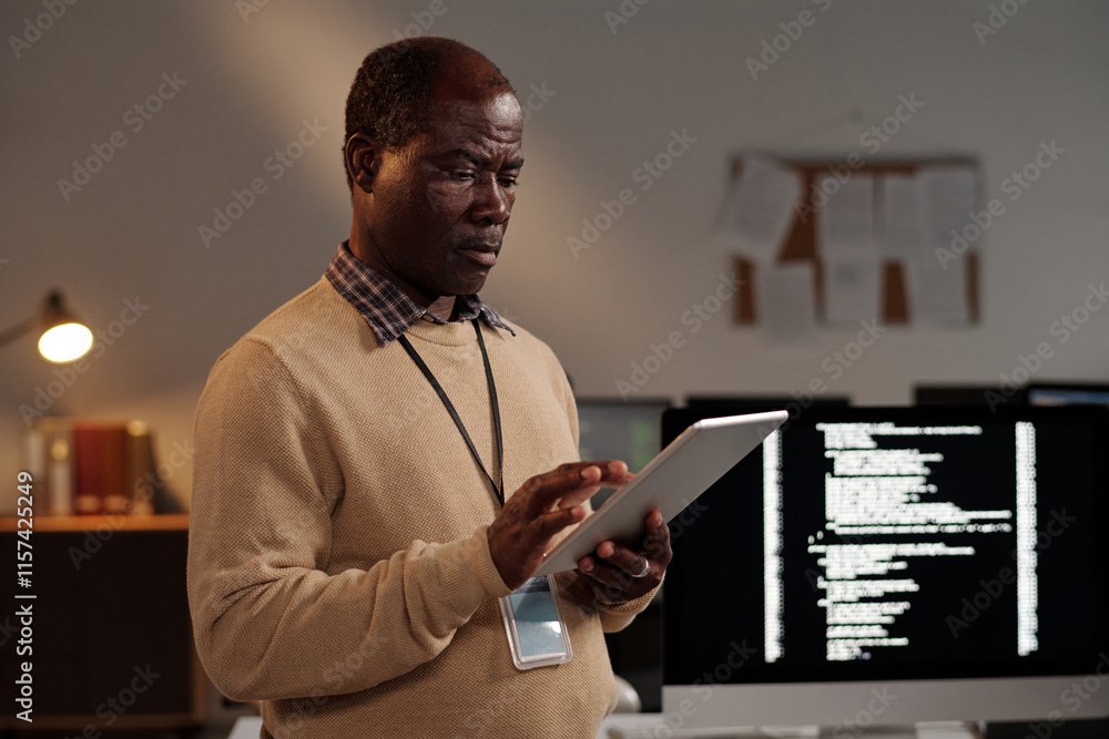 Poster Mature male IT engineer scrolling on tablet screen while decoding online data or testing new software in front of camera