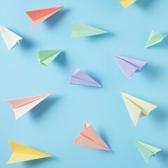 Fototapeta premium Pastel paper airplanes scattered on a light blue background.