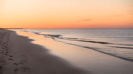 Obraz premium A photo of a serene beach at sunrise. The sky is painted with warm hues of orange and pink.