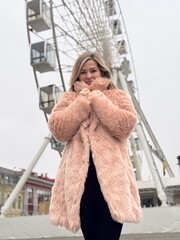 Outdoor portrait of young beautiful fashionable happy smiling girl wearing trendy pink faux fur...
