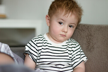 A small sick child looks sadly and tiredly with his brown eyes