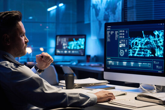 Young serious male operator in uniform looking at graphic data on computer screen while sitting by workplace