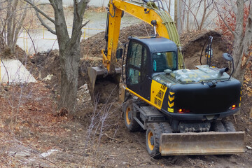 Soil pours out of the excavator bucket at a construction site surrounded by trees.