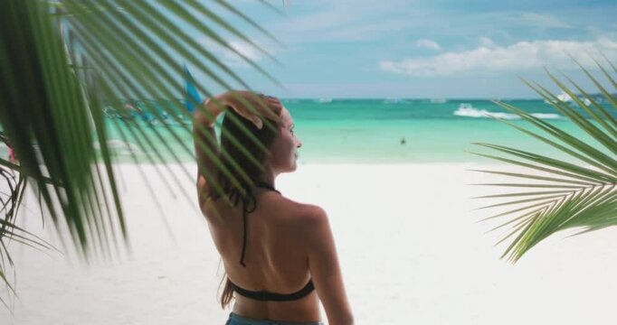 Young woman is taking in the idyllic scenery of a tropical beach, with white sand, turquoise water, and palm trees swaying in the breeze