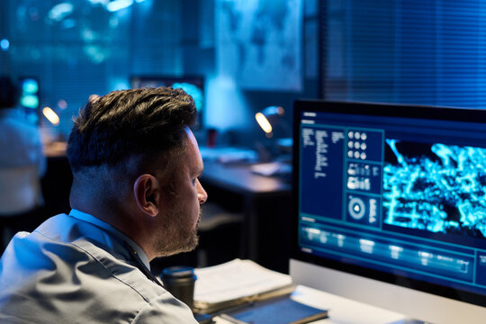 Focus on mature male officer in uniform sitting by workplace and looking at computer screen with graphic military data