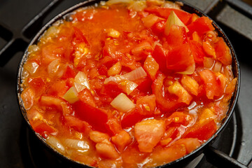 Tomatoes with pepper and onion are fried in a frying pan in oil