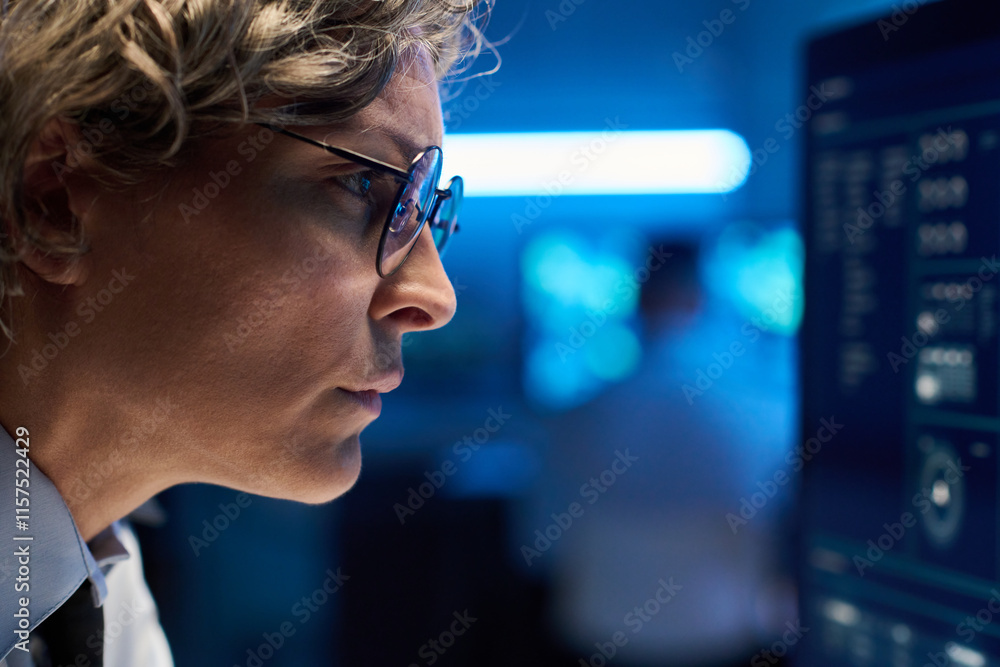 Leinwandbilder Side view of face of mature serious female operator in eyeglasses looking attentively at graphic data on desktop computer screen