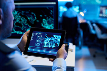 Digital tablet with graphic data on screen held by mature male operator in uniform sitting by...