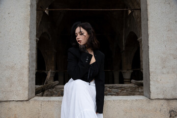 Young woman with black hair, dressed in black Gothic style, in a ruined church.