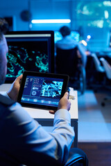 Male officer holding digital tablet with graphic data on screen while sitting by workplace and analyzing military location