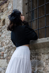 Young woman with black hair, dressed in black Gothic style, in a dilapidated church with barred windows.