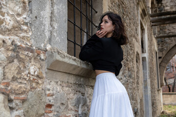 Young woman with black hair, dressed in black Gothic style, in a dilapidated church with barred windows.