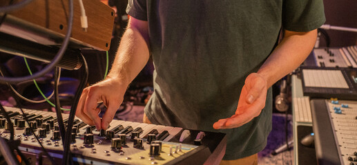 music producer adjusting knobs on a synthesizer in a recording studio 