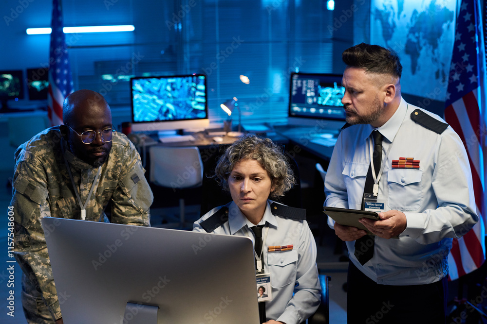 Poster team of serious workers of military command center looking at online data while sitting and standing