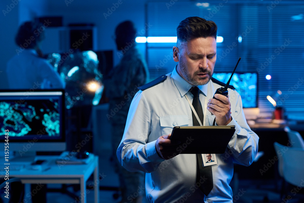 Aufkleber mature man in uniform looking at tablet screen and speaking in walkie-talkie while reporting about m