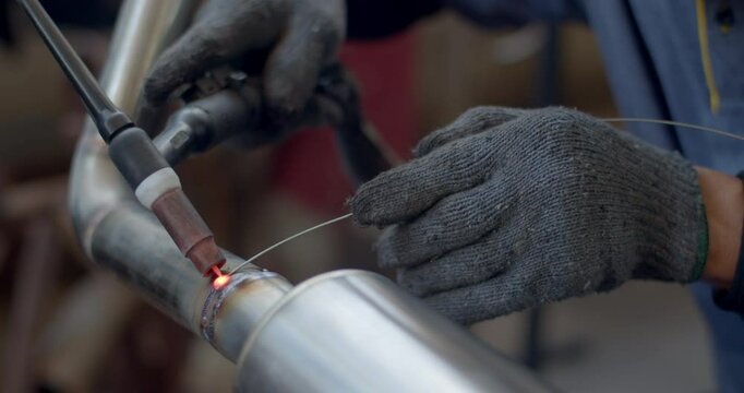 Close up tig welding.Car pipe welding.Automotive exhaust pipe welding with wire filling.The hand of a mechanic or welder is fixing a car exhaust system.Tig welding makes the welds come out beautiful.
