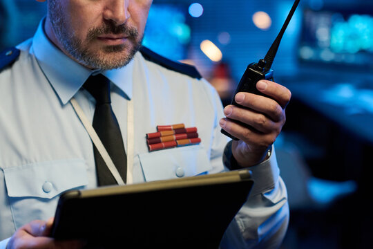 Hand of male officer in uniform holding tablet and walkie-talkie during report of military situation from command center - Powered by Adobe