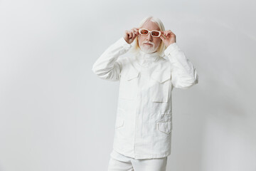 Elderly man in stylish white outfit with trendy glasses, standing against a plain white background,...
