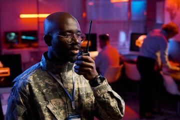 Young confident African American male officer in camouflage uniform speaking in walkie-talkie in military command office