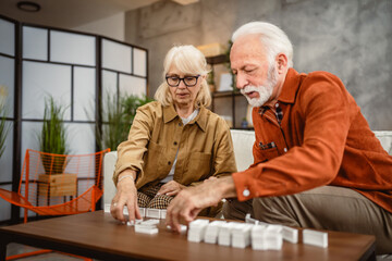 Senior happy couple husband and wife play dominoes together at home