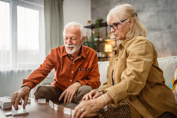 Senior happy couple husband and wife play dominoes together at home