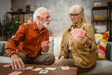 senior couple husband and wife play cards at home in bright day