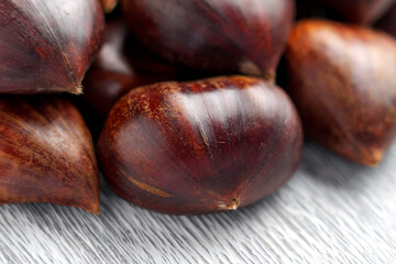 Group of fresh whole chestnuts with glossy nut shells arranged on a gray textured surface. Close up